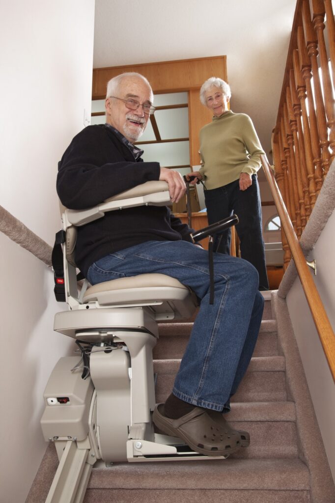 Old Man using his new stairlift installed by AMS group Ltd with his wife watching